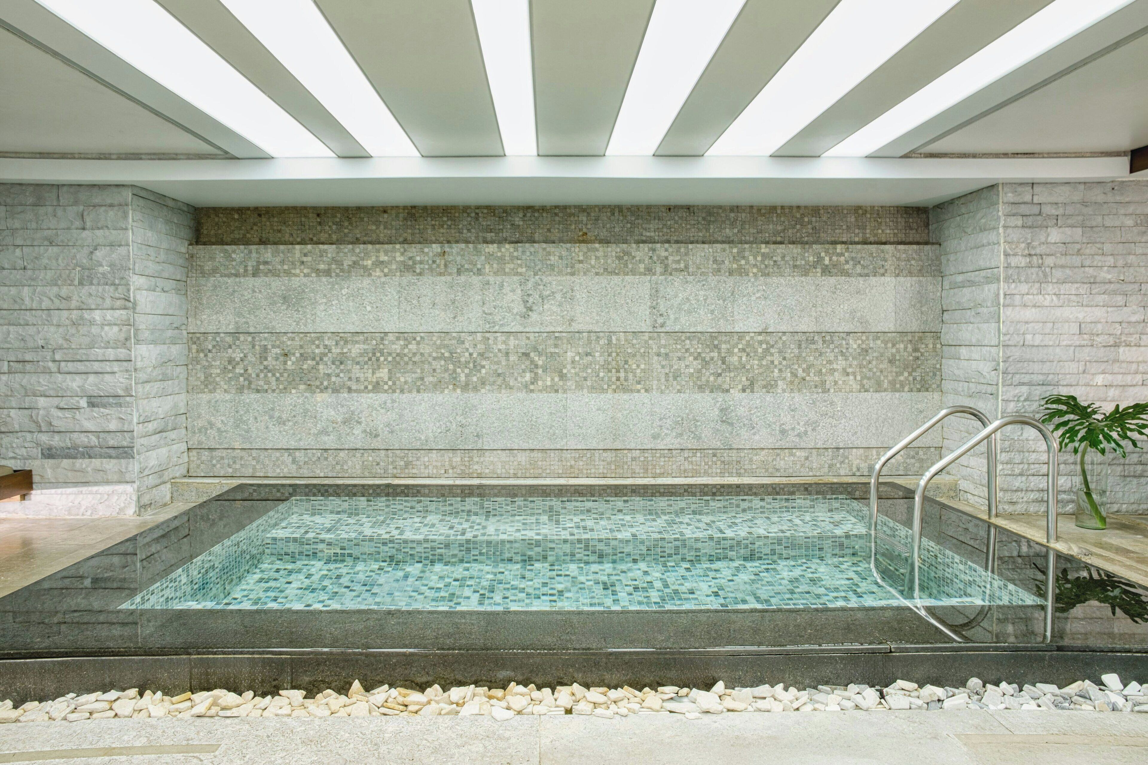 A modern indoor pool with clear water, stone walls, and a metal ladder.