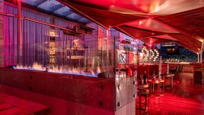 Zona de bar moderna con chimenea, divisiones de vidrio y suelo de madera.