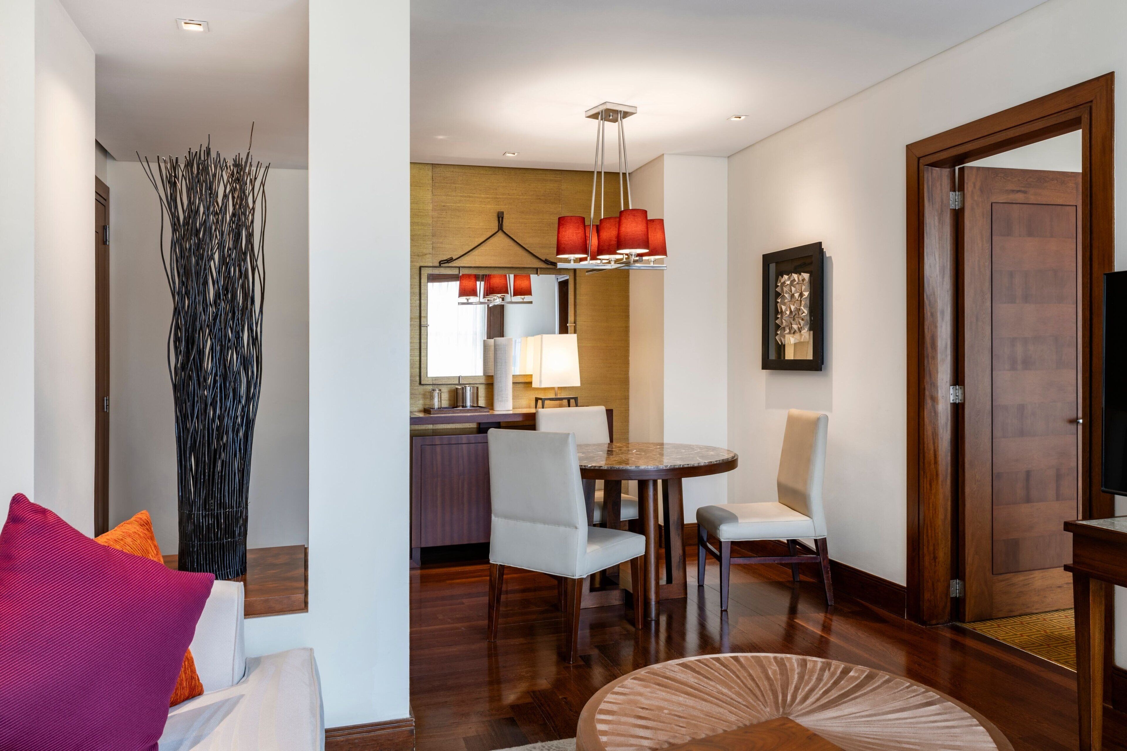 A modern hotel room with a dining area, a living space with a sofa and a coffee table, and a wooden door.