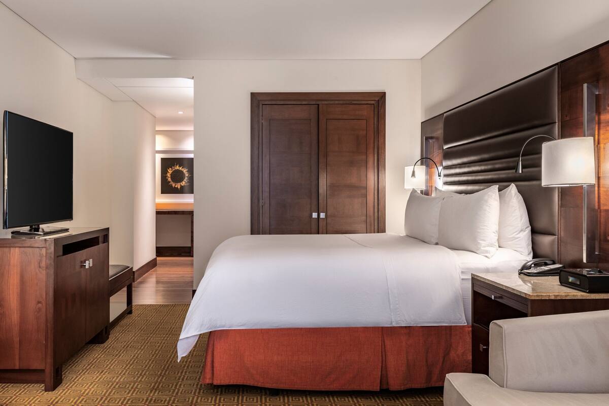 A hotel room with a large bed, a desk with a telephone, a television, and a wardrobe.
