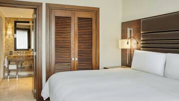 A hotel room with a large bed, wooden wardrobe, a bathroom with a vanity, and a mirror.