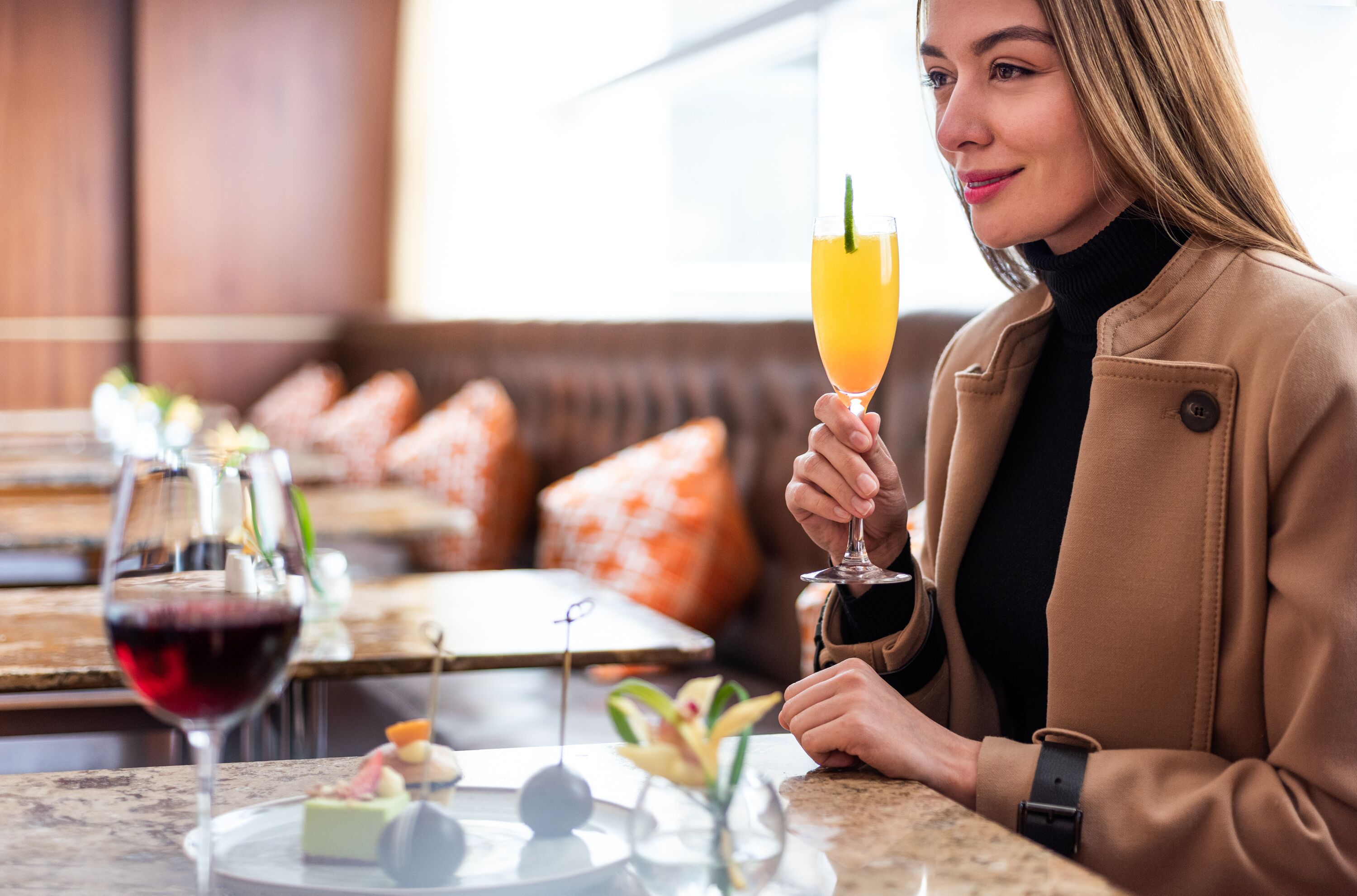 A person holding a glass of orange juice at a restaurant with a dessert plate and a glass of red wine on the table.