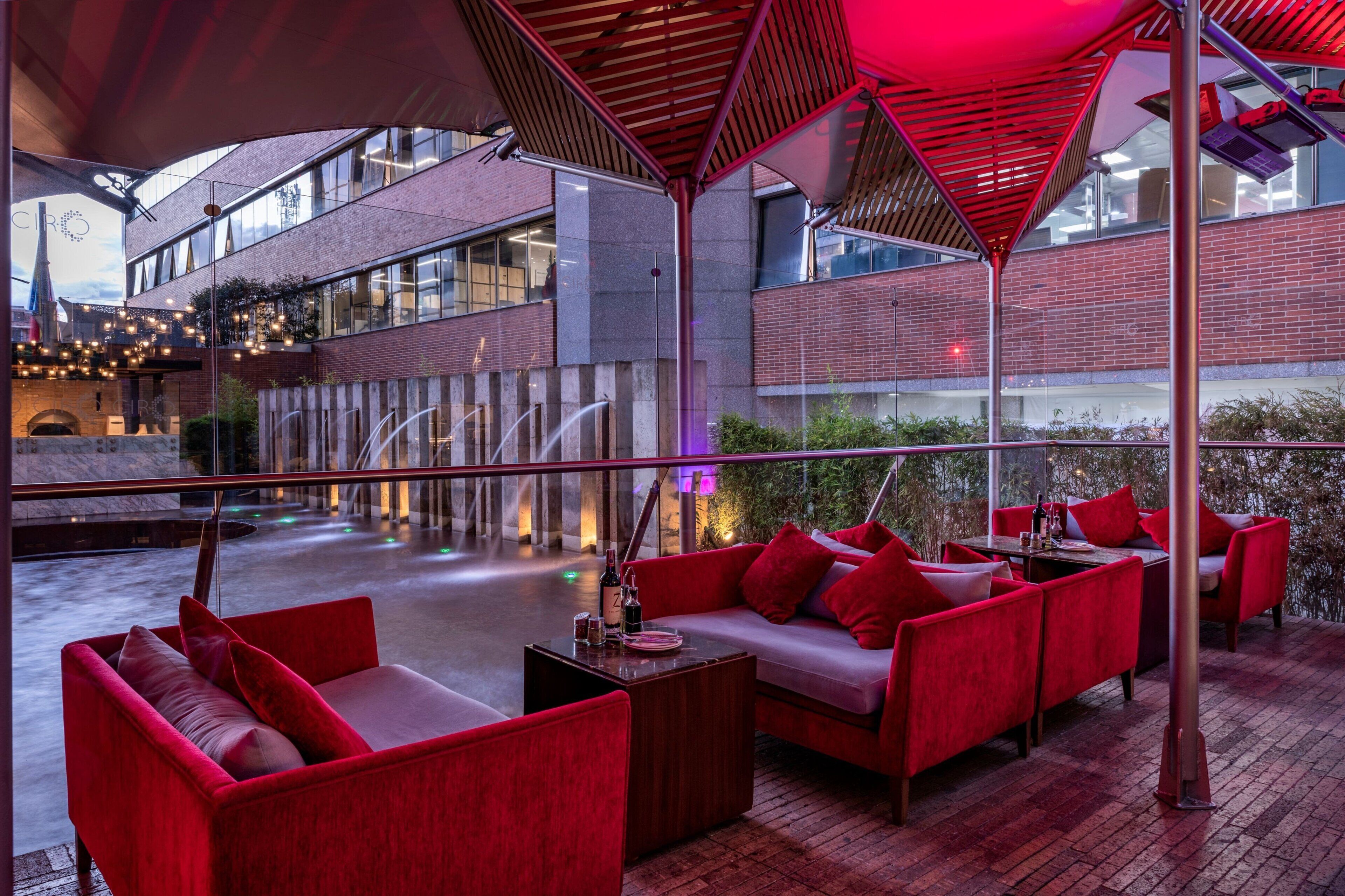 A modern indoor lounge with red seating, a pool, and a view of the building's exterior.
