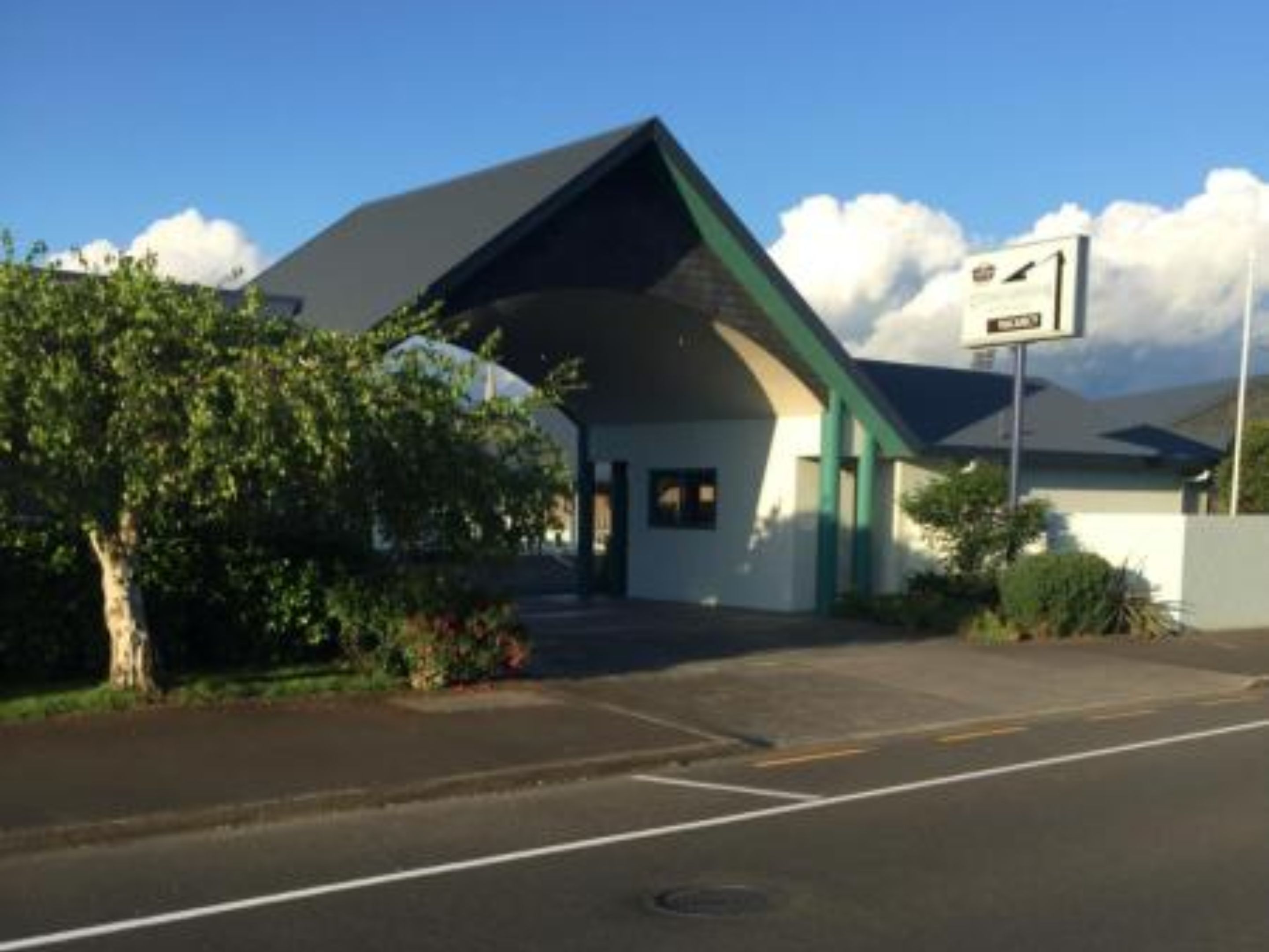 A building with a sloped roof, a signboard, and a tree in front.