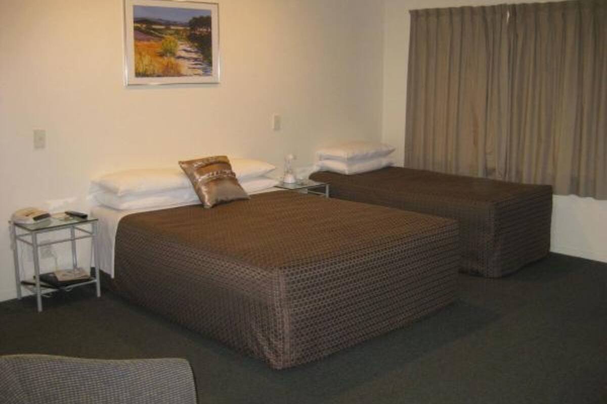 A hotel room with two beds, a small table, a chair, and a painting on the wall.