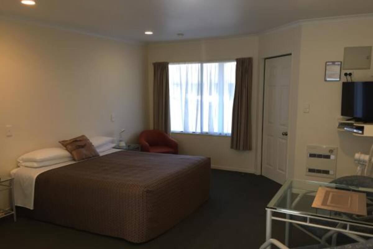 A hotel room with a bed, a chair, a desk with a computer, and a television.