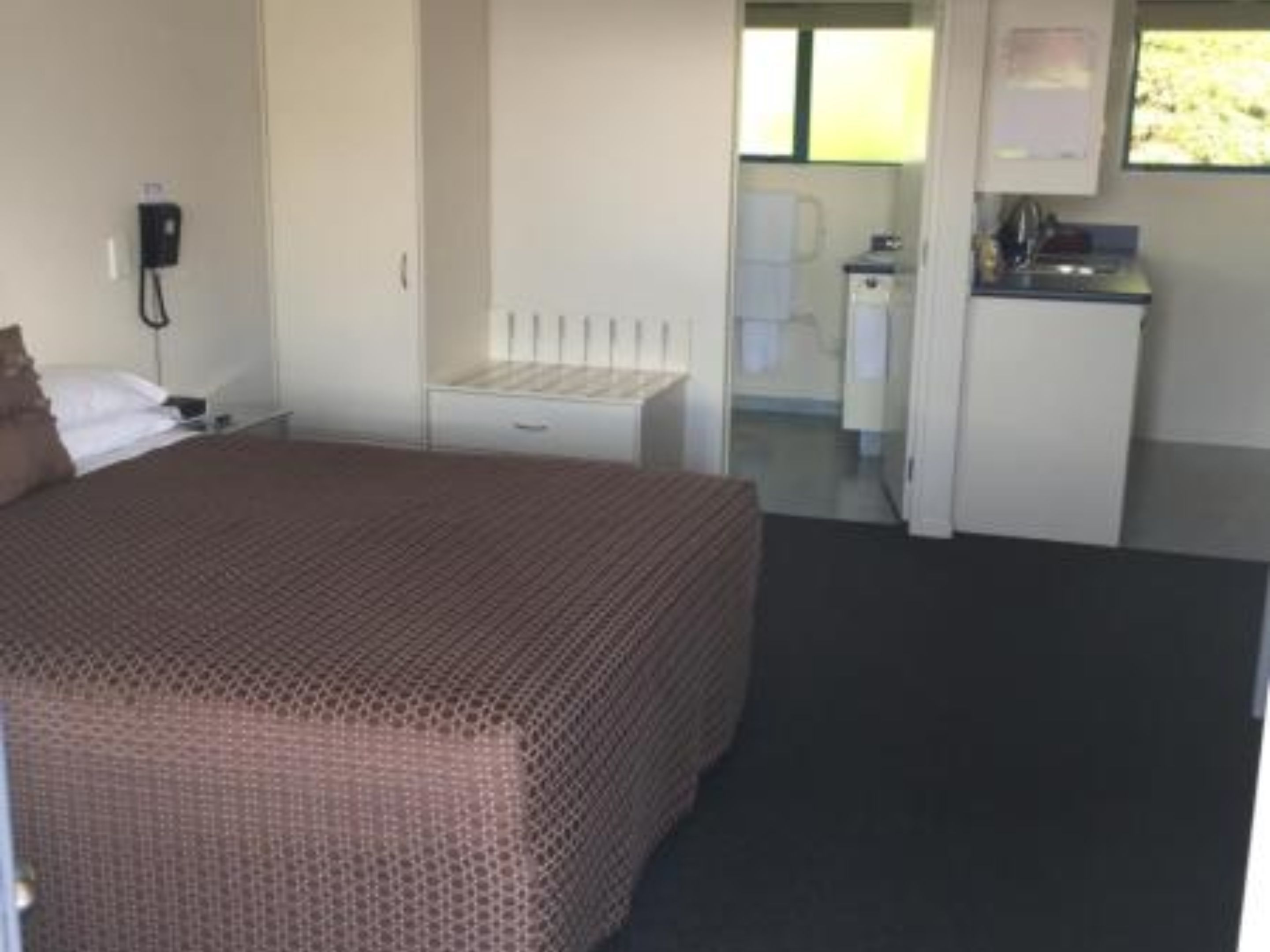 A bedroom with a bed, a bedside table, a small desk, and a window.