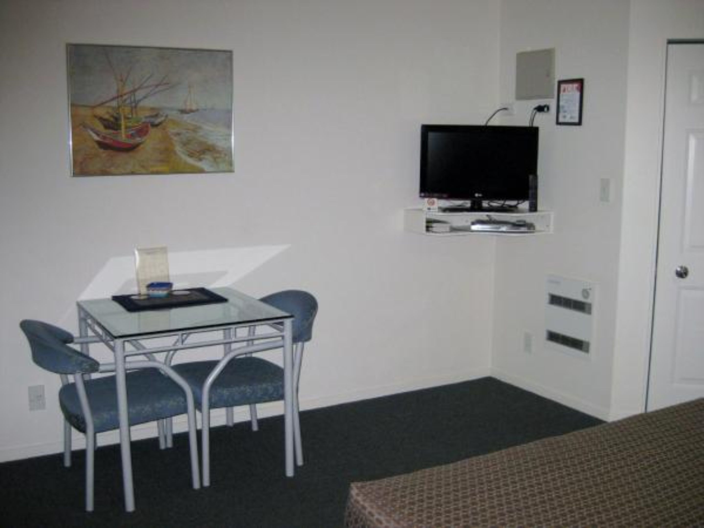 Une petite pièce avec un lit simple, un bureau avec deux chaises, une télévision et un tableau accroché au mur.