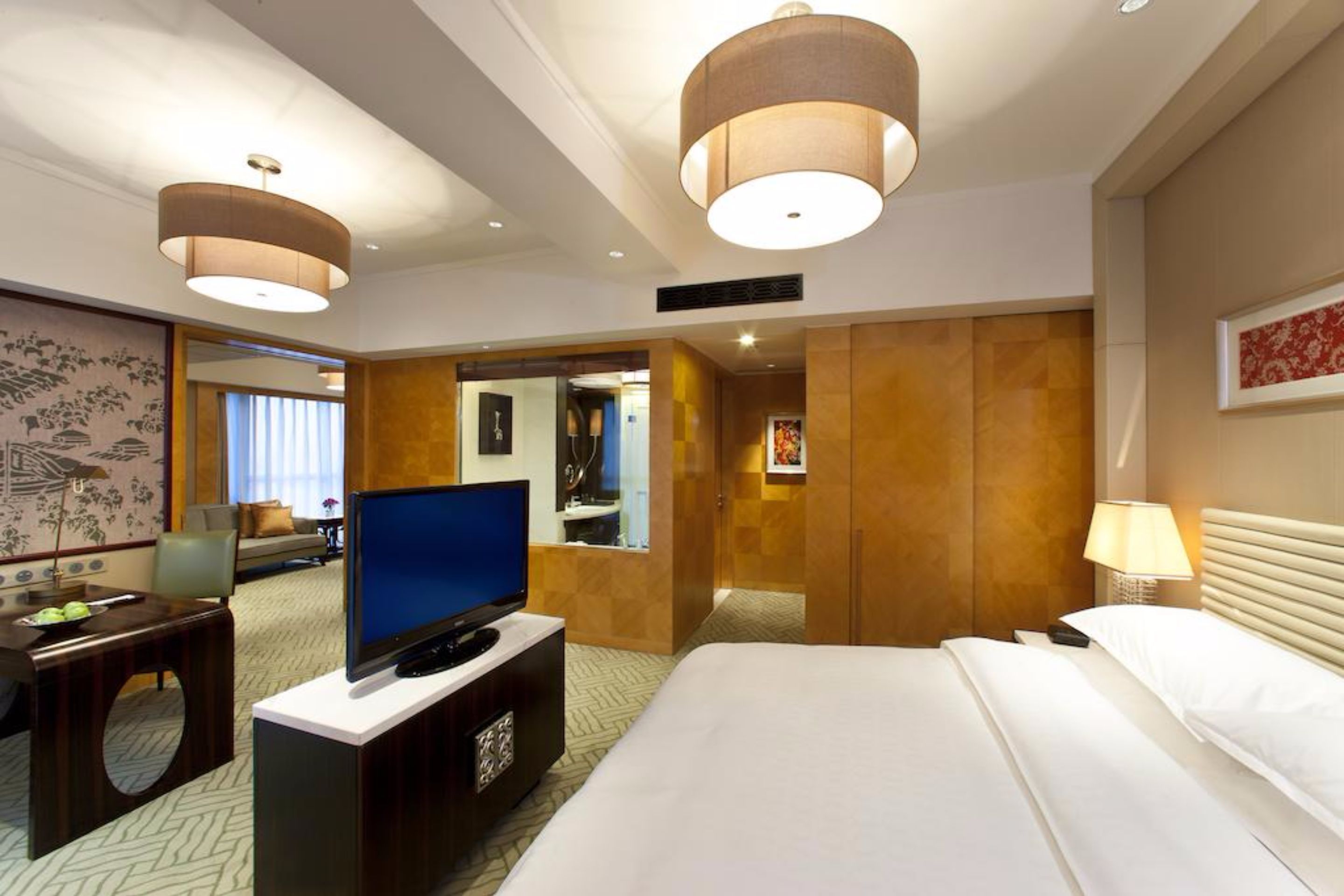 A hotel room with a bed, a television on a stand, a desk with a chair, and a large mirror.