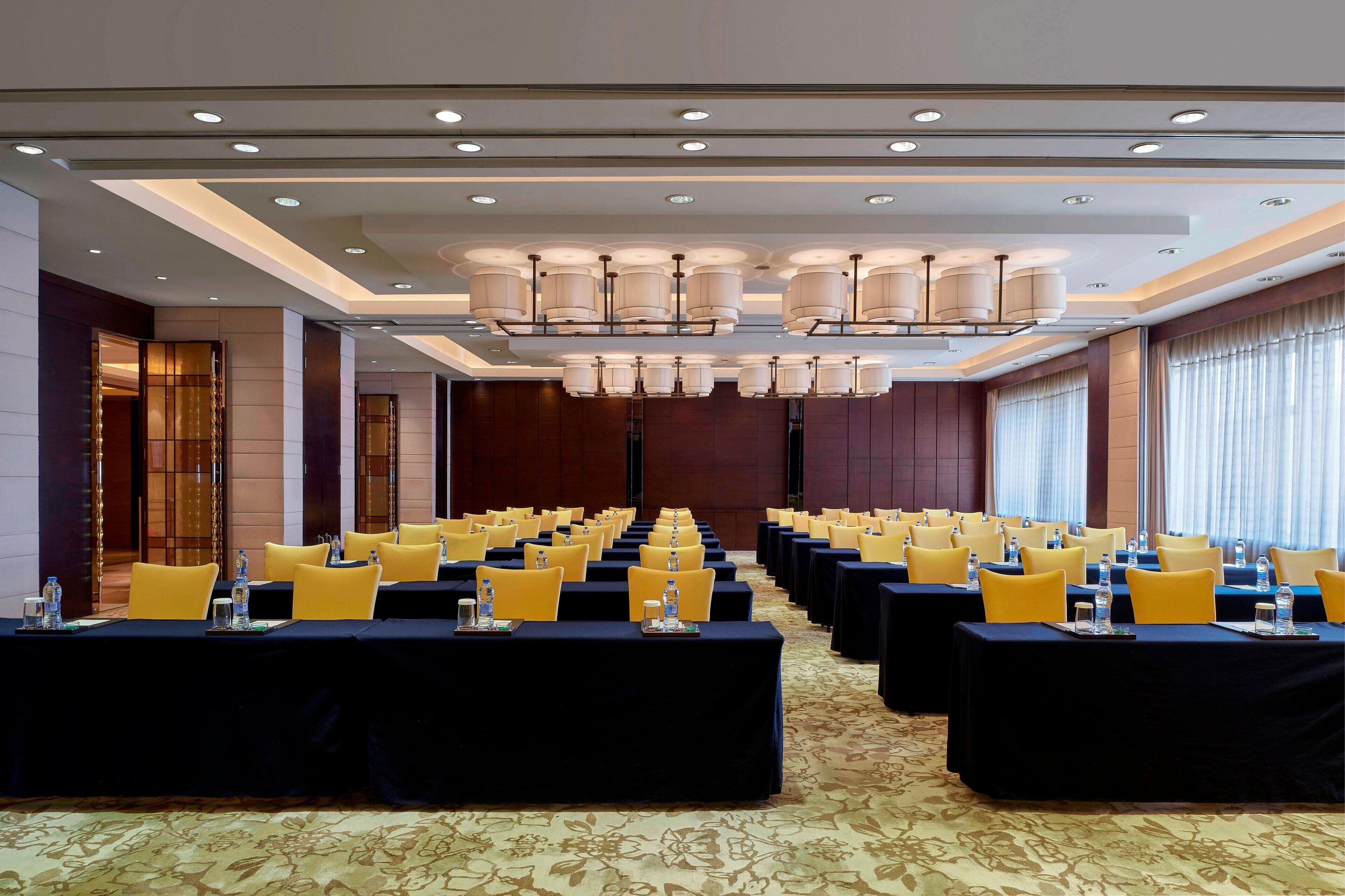 A conference room with rows of tables, yellow chairs, and a chandelier.