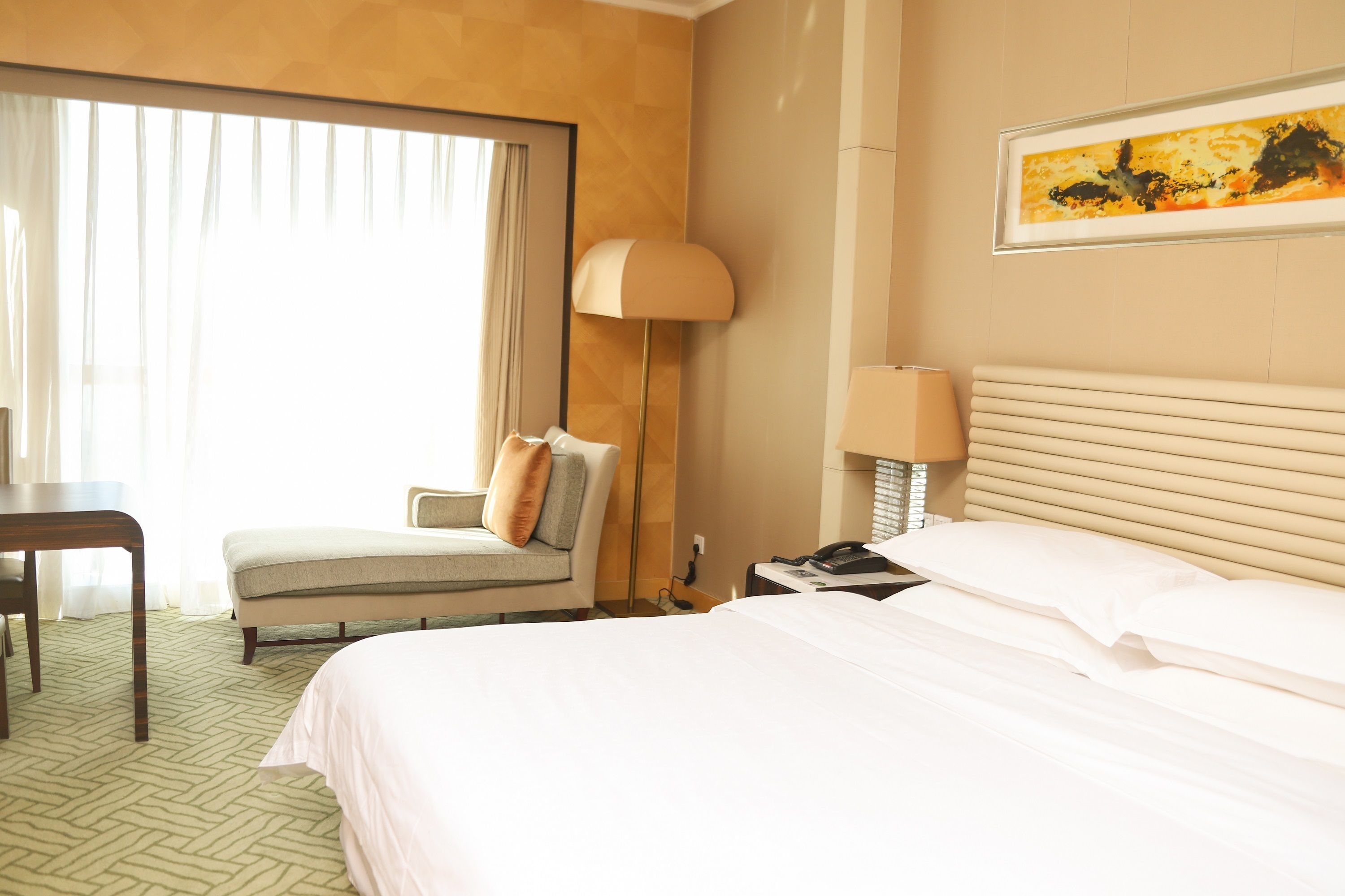 A hotel room with a large bed, a desk, a chair, a lamp, and a painting on the wall.