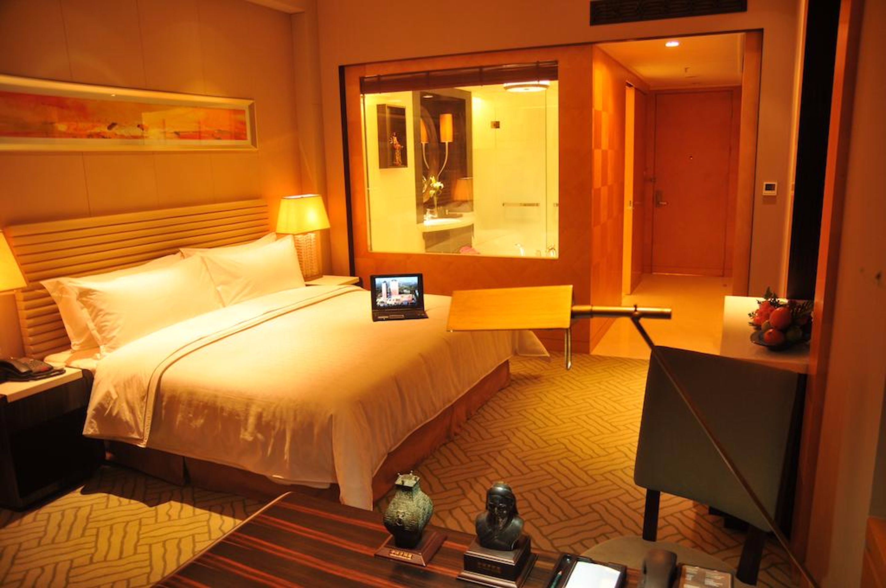 Een hotelkamer met een bed, nachtkastje, lamp, spiegel en een klein bureau met stoel.