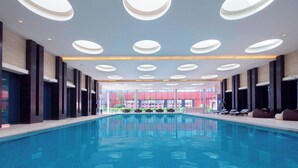 Une piscine intérieure moderne, dotée d’un espace de repos central et de plusieurs luminaires au plafond.