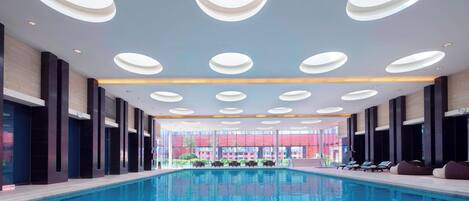 Una piscina interior moderna con una zona de estar central y varias luces en el techo.