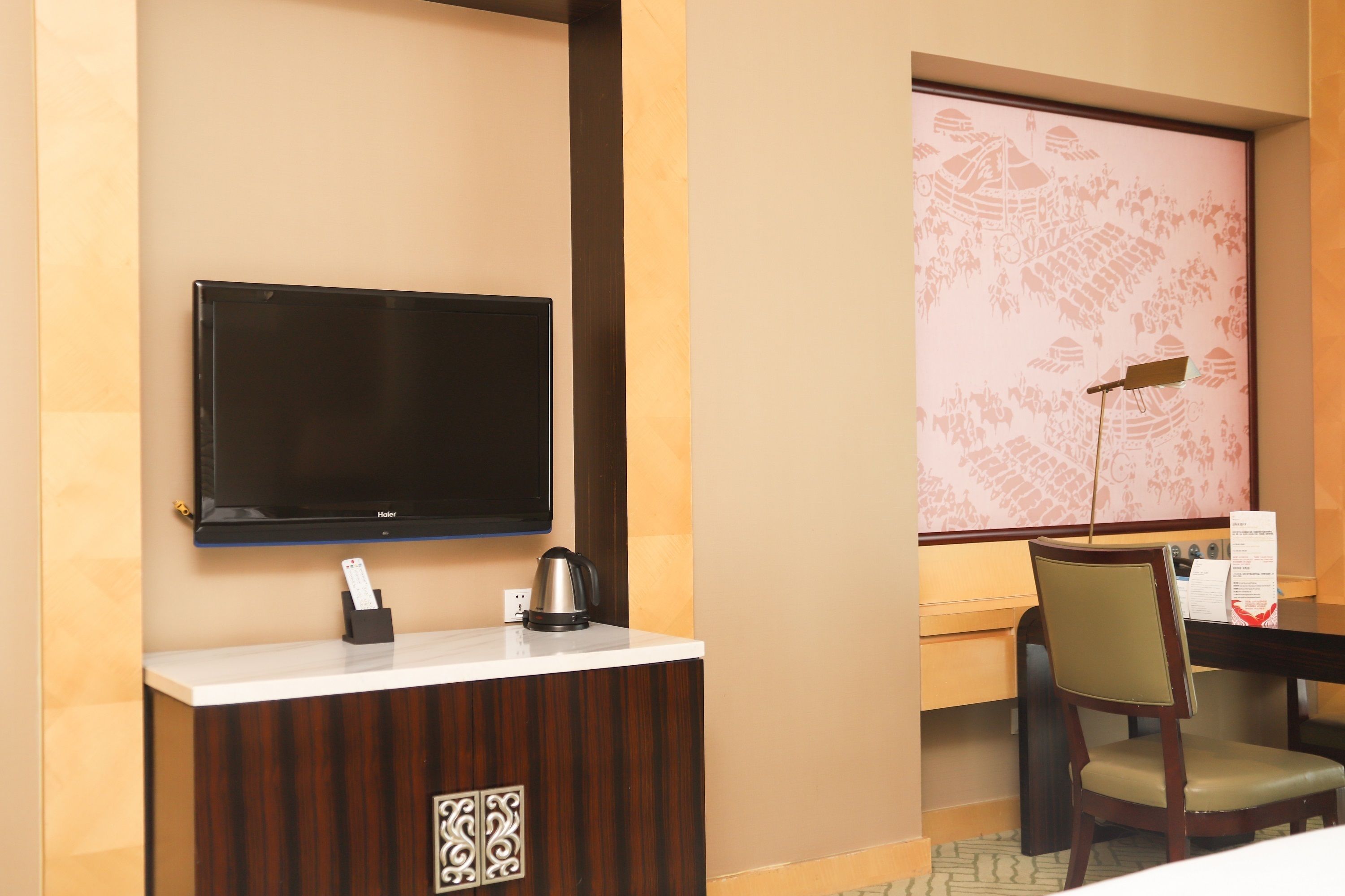 A hotel reception area with a flat-screen TV, a coffee maker, a desk, and a chair.