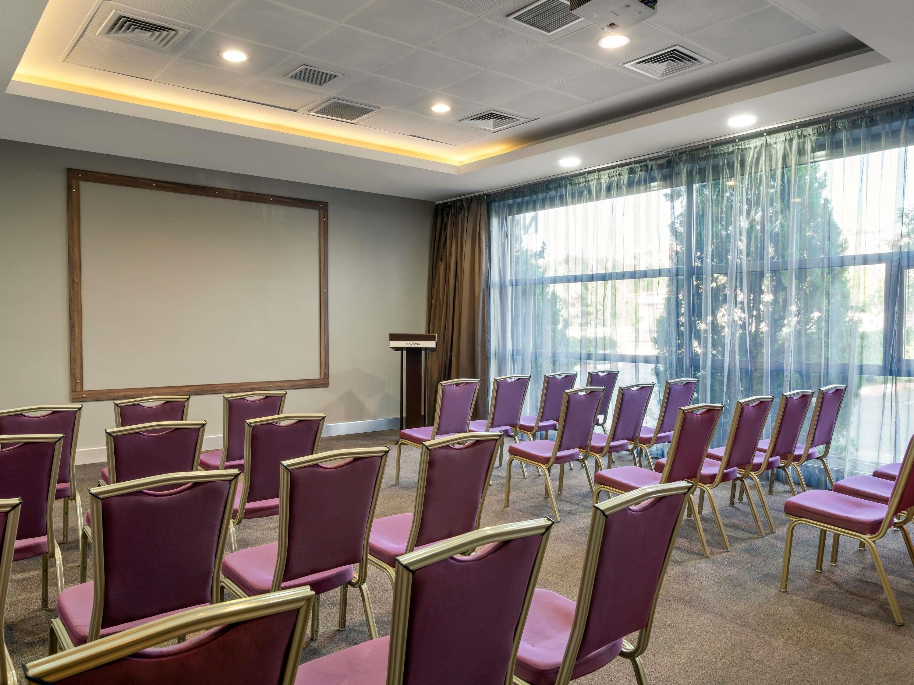 A conference room with rows of purple chairs, a projector screen, and a podium.