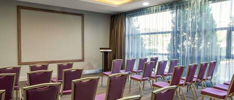 Un salón de conferencias con filas de sillas moradas, una pantalla de proyector y un atril.
