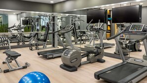 Een moderne sportschool met diverse cardioapparaten, gewichthefapparatuur en een grote spiegel die de ruimte weerspiegelt.