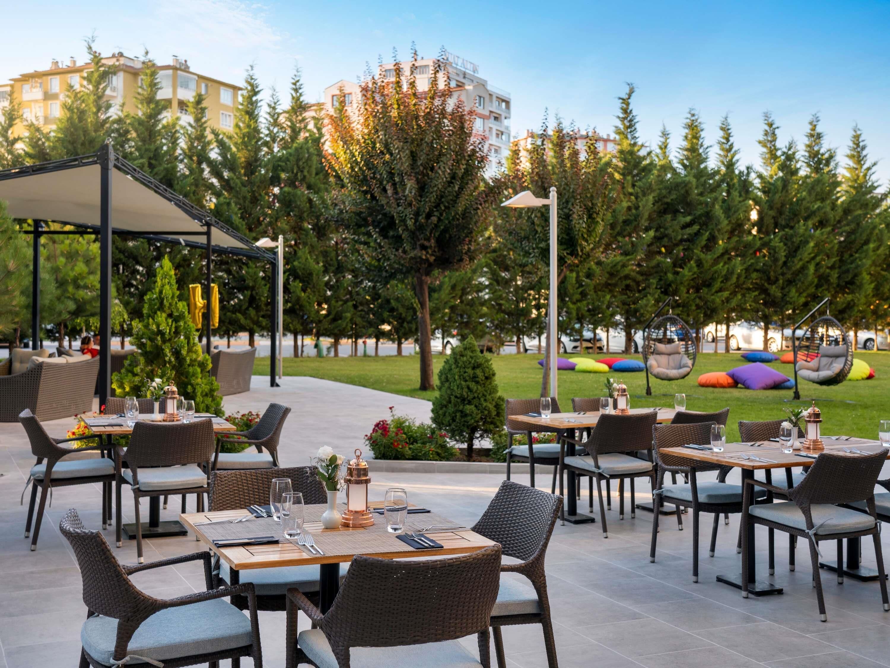 An outdoor dining area with wicker furniture, tables set with cutlery and glasses, and a Christmas tree.