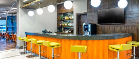 A modern bar area with a curved counter, multiple bar stools, and a television mounted on the wall.