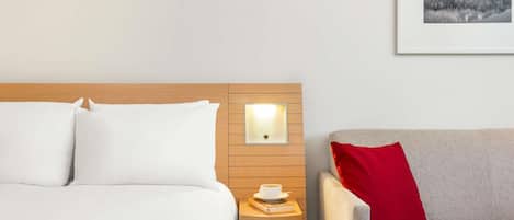 A hotel room with a bed, a nightstand with a lamp, a chair, and a framed picture on the wall.