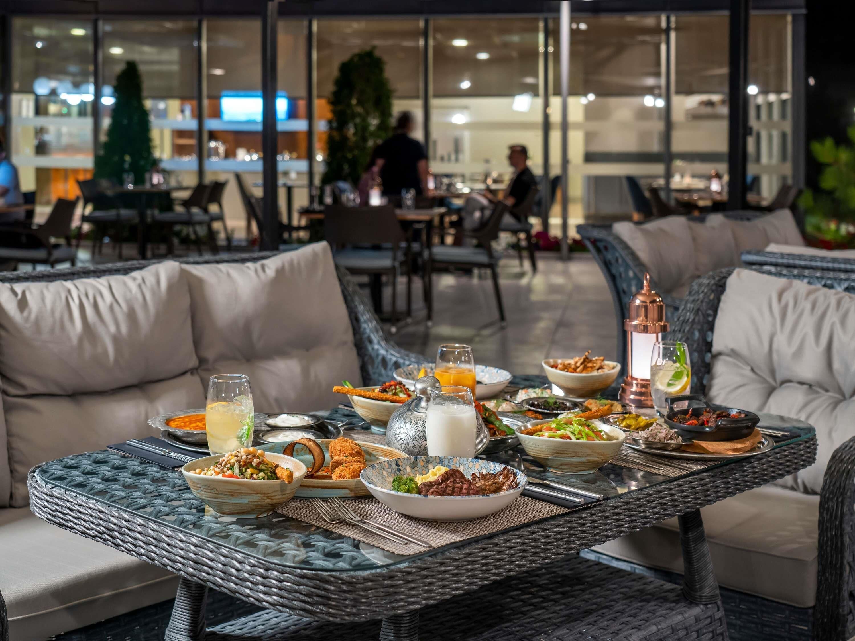 An outdoor dining area with wicker furniture, multiple dining tables, and a variety of dishes.