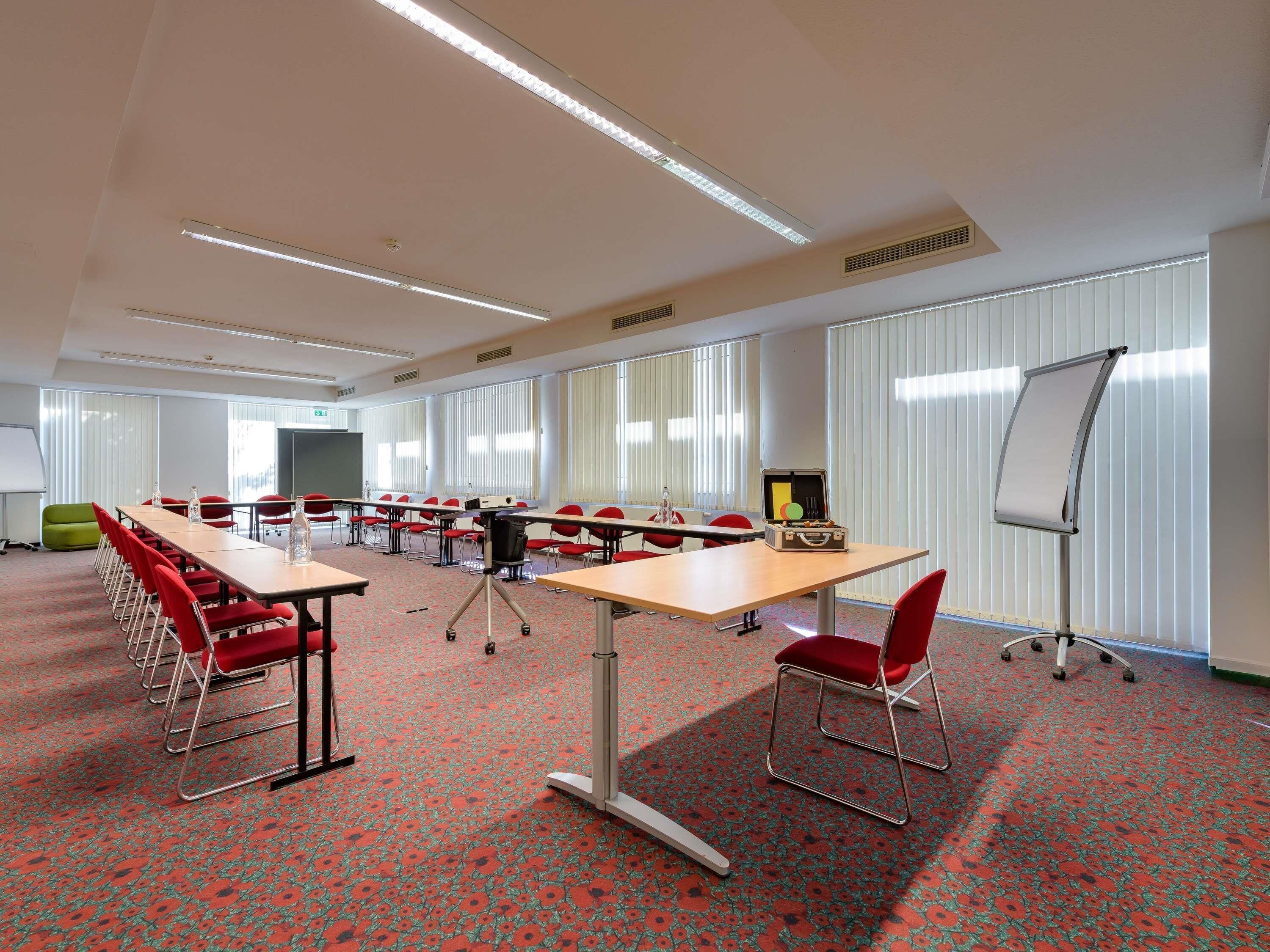 Ein Konferenzraum mit einem langen Tisch, roten Stühlen, einem Projektor und einer Whiteboard.