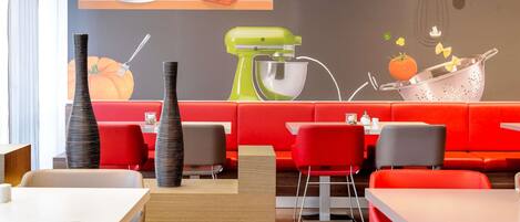 Un interior de restaurante moderno con asientos rojos, una zona de cocina con un mezclador y una pared con utensilios de cocina y una decoración de calabaza.