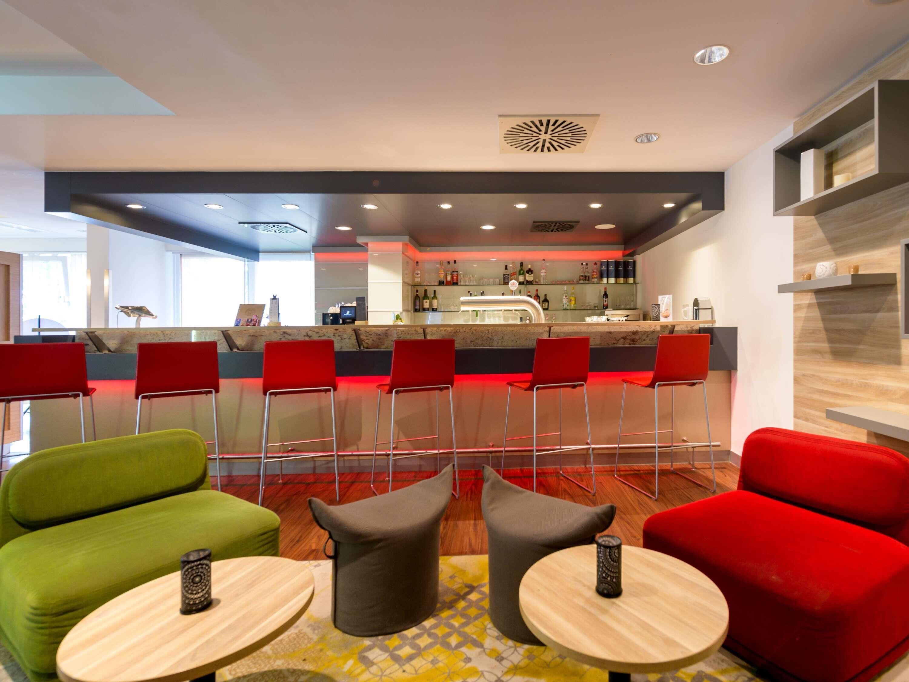 A modern bar area with red chairs, a green sofa, and a bar counter with various bottles.