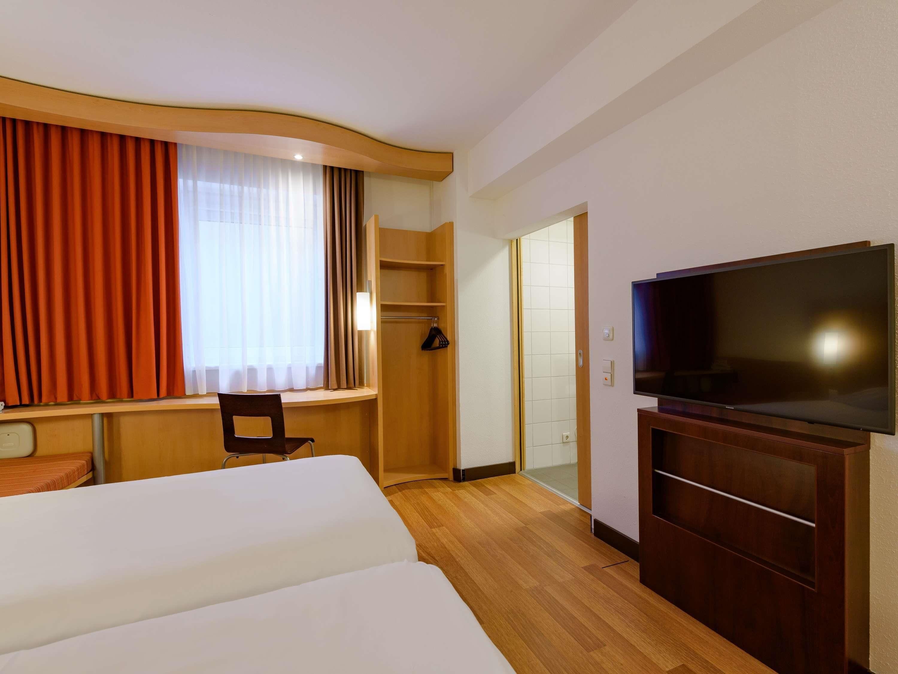 A hotel room with a bed, a desk, a television, and a wardrobe.