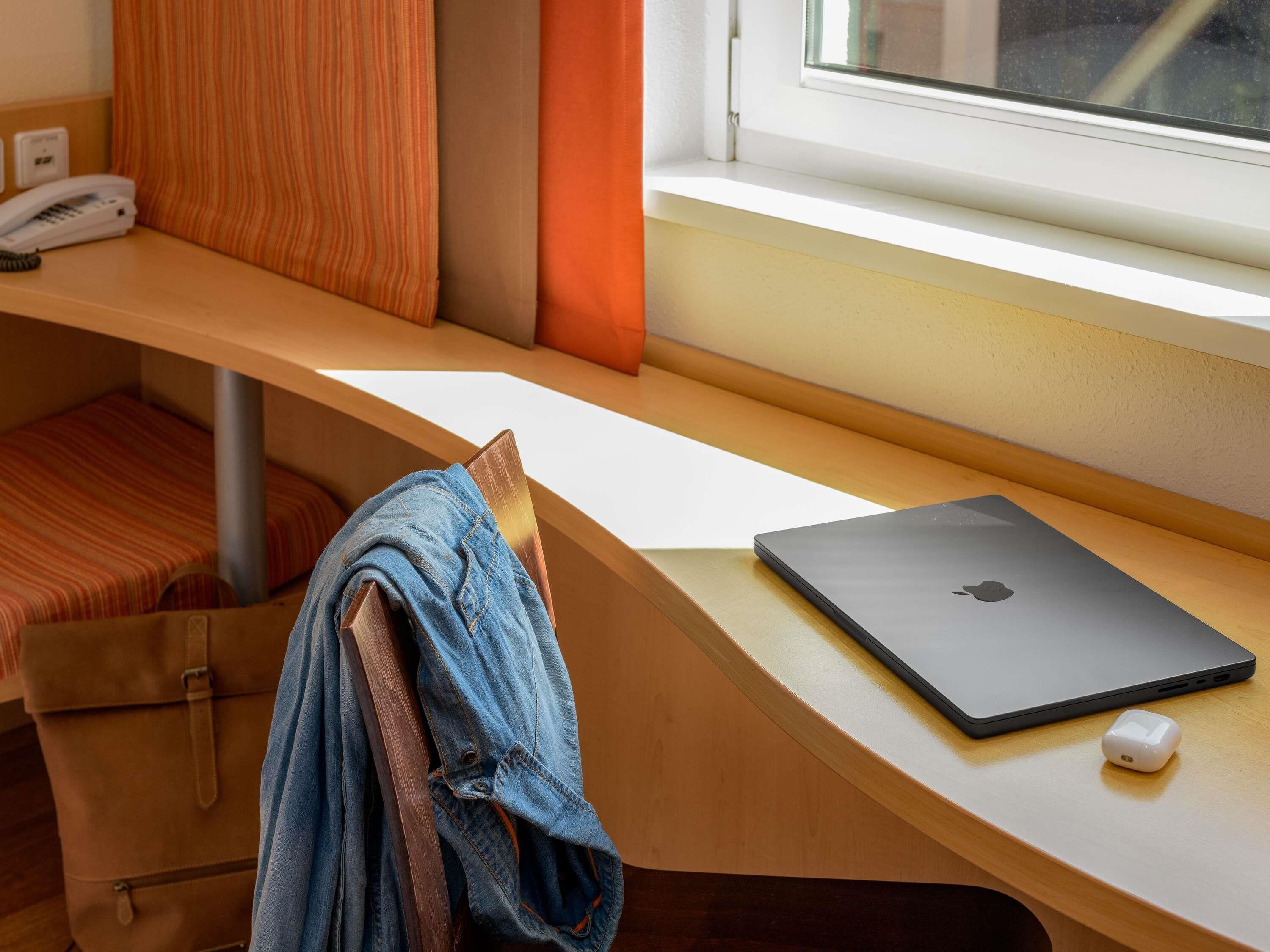 Habitación de hotel con escritorio de madera, una computadora portátil, un dispositivo de carga blanco y un cojín a rayas.