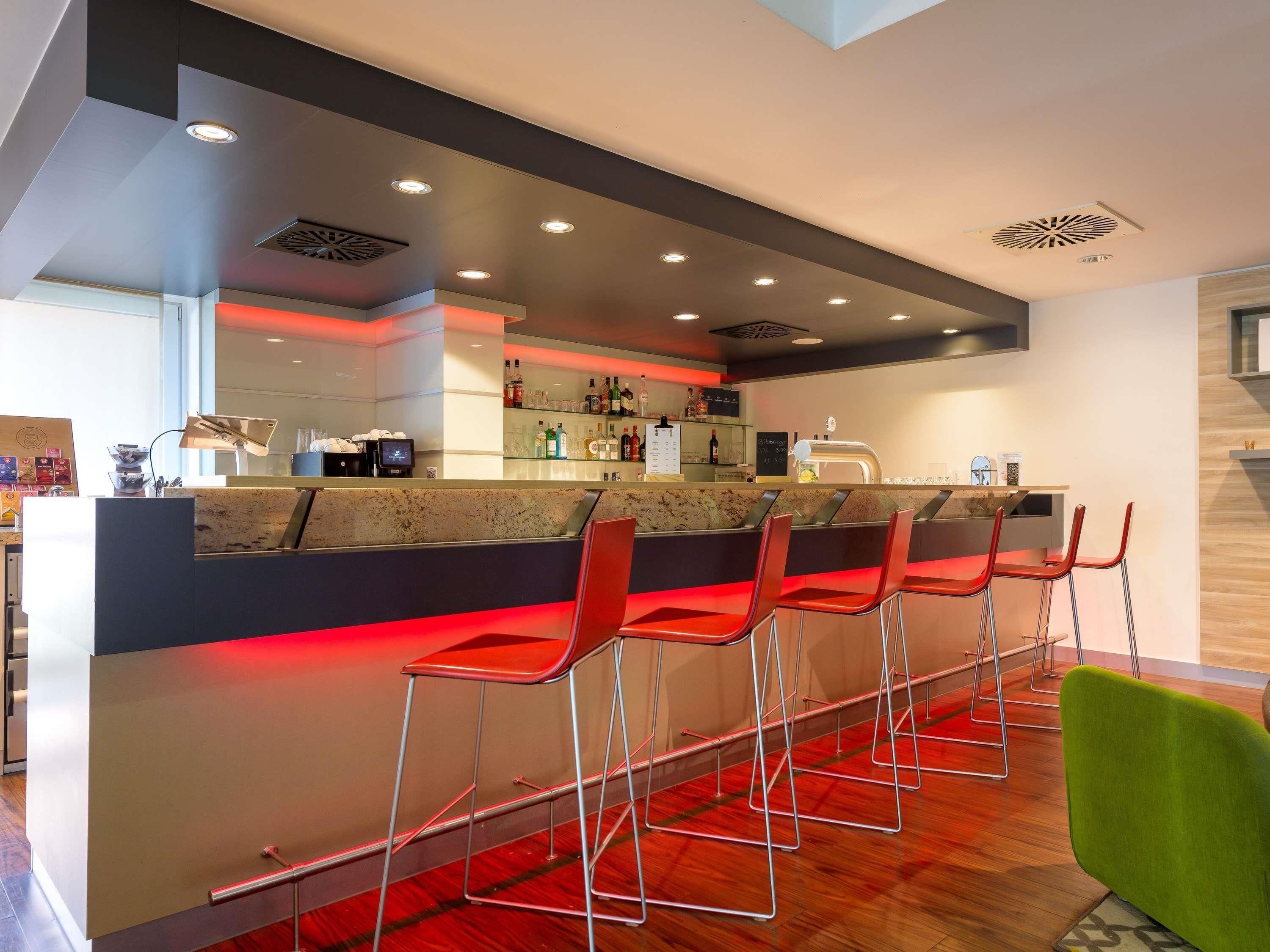 A modern bar area with a counter, red bar stools, and a green chair.