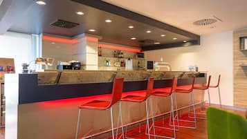Un espace bar moderne avec un comptoir, des tabourets de bar rouges et un fauteuil vert.