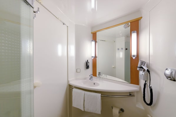 Un baño con lavamanos blanco, un espejo, toallero, secador de pelo y ducha.