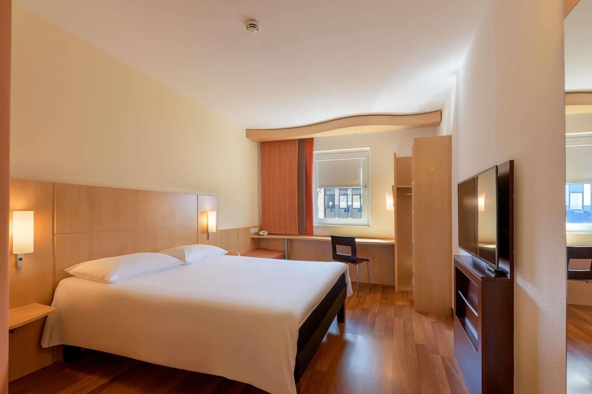 Une chambre d’hôtel avec un grand lit, un bureau, une chaise, une télévision et une fenêtre donnant sur un beau paysage.