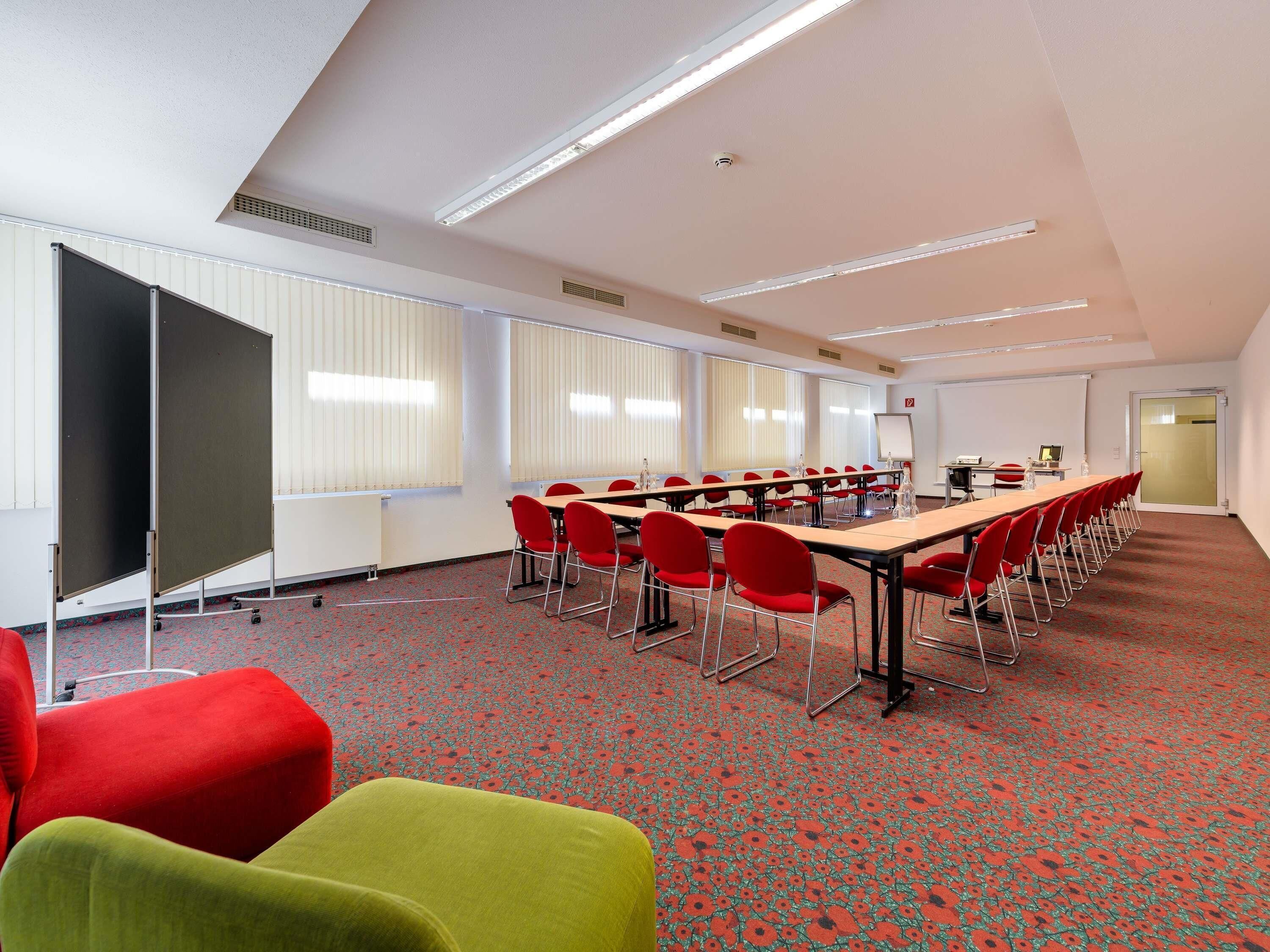 A conference room with a long table, red chairs, a projector screen, and a whiteboard.