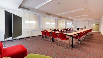 A conference room with a long table, red chairs, a projector screen, and a whiteboard.