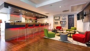 Zona de bar moderna con barra, taburetes rojos y un área de estar con sillas verdes y rojas.