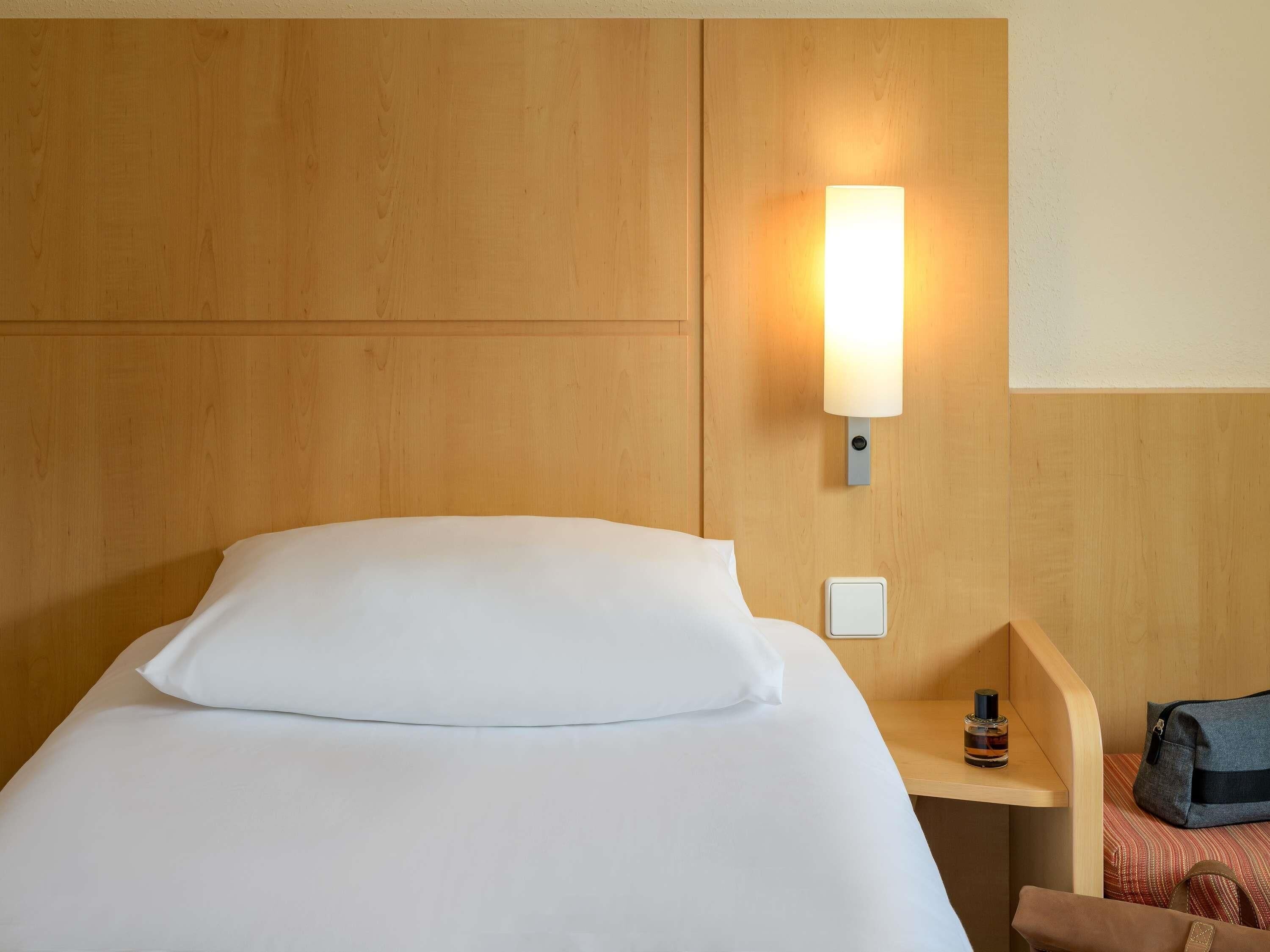 Ein Hotelzimmer mit Bett, Nachttisch, Lampe und einem an der Wand befestigten Lichtschalter.