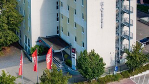 Un edificio de varios pisos con un llamativo logotipo de ibis, una escalera que conduce a la entrada y un asta con la bandera de ibis.