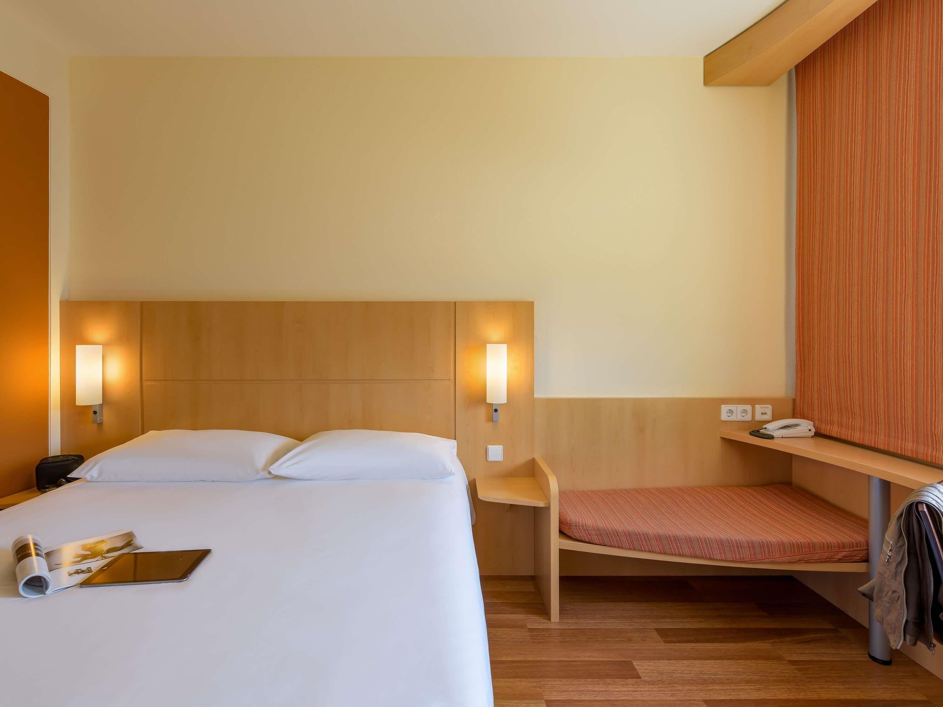 Una habitación de hotel con cama, mesita de noche y un pequeño rincón de descanso.