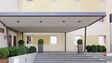 A hotel entrance with a covered walkway, steps, and potted plants.
