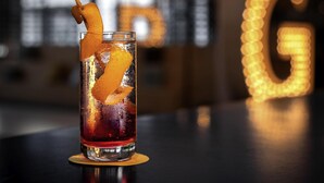 Een cocktail met een oranjesnipper, geplaatst op een onderzetter.