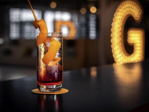 Een cocktail met een oranjesnipper, geplaatst op een onderzetter.