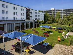 Een binnenplaats met buitenmeubilair, een barbecuehoek en een gebouw met meerdere verdiepingen op de achtergrond.