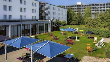 Un patio con mobiliario exterior, zona de barbacoa y un edificio de varios pisos al fondo.