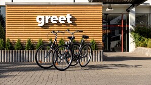Een gebouw ingang met een 'greet' bord en twee fietsen er voor.