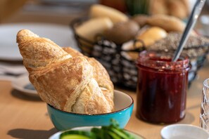 Un croissant dans un bol bleu, un pot de confiture et un panier de pain sur une table.