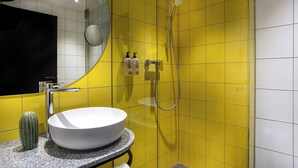 Een badkamer met een wit wastafelmeubel, gele tegels, een douche en een spiegel.
