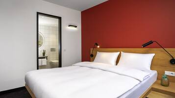 A hotel room with a bed, a nightstand, a wall-mounted lamp, and a mirror.